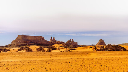 Tadrart Rouge, Djanet, Illizi. Orange color reg stones, sandstones. Blue covered sky. Panoramic view of Sahara Desert sand dune and rocky mountains with awesome human shapes like a family sitting down