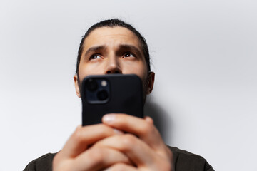 Close-up portrait of thoughtful man with smartphone in hands, looking up.