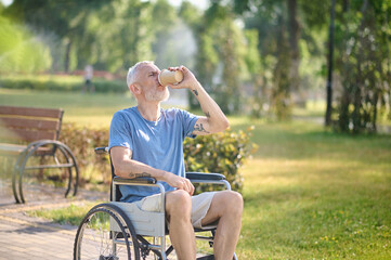 Obraz premium A man in a wheel chair sitting in the park and having coffee