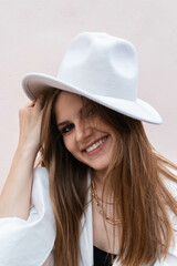 a girl in a white shirt and a white hat is sitting at a pink background