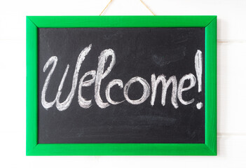 Welcome, written in chalk on a black chalkboard in a green frame.
