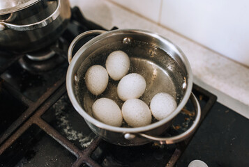 Chicken white eggs are boiled in boiling water in a metal saucepan.
