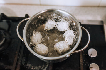 Chicken white large eggs are boiled in boiling water in a metal saucepan on the stove in the kitchen. Morning breakfast, food photography, concept.