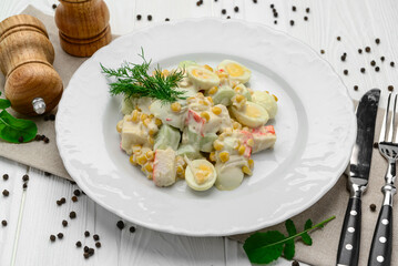 Salad with crab sticks, sweet corn, cucumber, eggs and mayonnaise on light table.