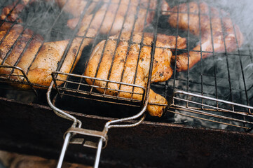 Chicken thighs are fried on the grill in a barbecue on a fire with smoke in nature.