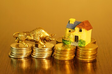 A metal bull and a toy house on a stack of coins.