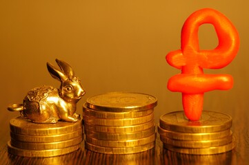 A metal rabbit figurine and a ruble symbol with coins. Economics and finance.