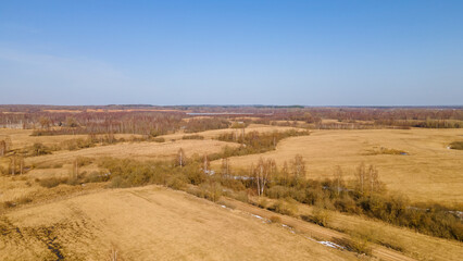 Aerial view of fields with copse, dry yellow grass, a stream, remnants of snow in early spring. Nature background.