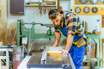 Handsome carpenter preparing, measures and cutting boards on cutting machine