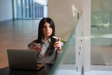 Fototapeta premium A young woman drinks coffee and works on a laptop on a food court
