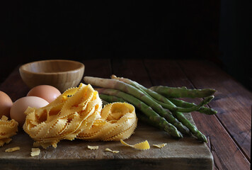 Cucina italiana. Pappardelle di pasta fatta in casa, uova e asparagi isolati su fondo di legno....