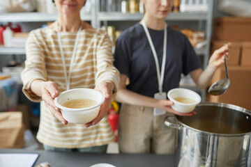 Close up of two female volunteers giving out simple meals to people in need at soup kitchen of help center
