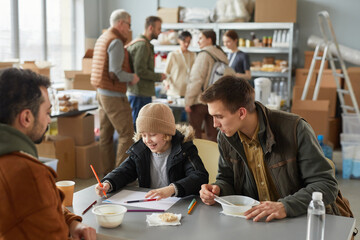 Portrait of Caucasian father and son enjoying simple meal at soup kitchen or help center for...