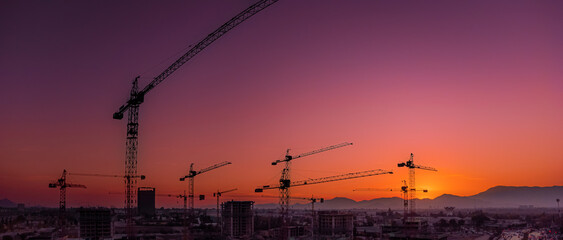 Grúas pluma, trabajan y operan en la construcción con cálido atardecer de fondo. Cielos...
