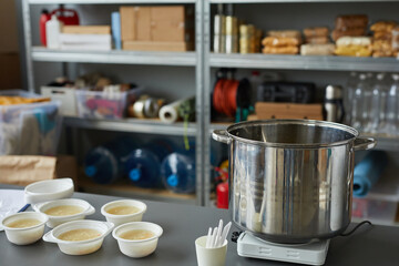 Background image of large saucepan with bowls on table in soup kitchen or help center for refugees,...