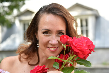 beautiful brunette woman with red roses near the bush in the park