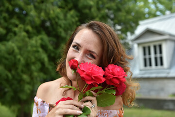 beautiful brunette woman with red roses near the bush in the park