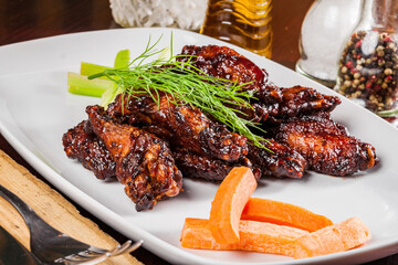 Buffalo chicken wings with crunchy vegetables on a white plate. Close up