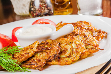 Zucchini fritters with sour cream, tomato and dill on a white plate