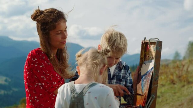 Positive family painting in mountains. Mother children creating artwork outdoor