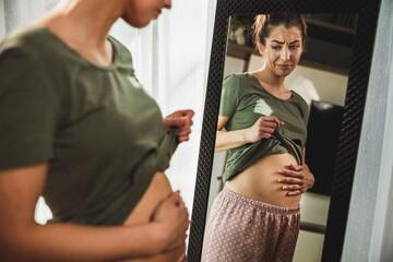 Woman Touching Her Belly While Standing Near Mirror