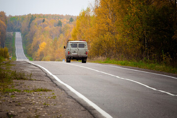 Fototapeta na wymiar An old car rides along asphalt road in the autumn forest