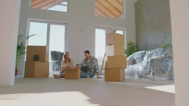Couple opening boxes afte moving into a new apartment. Discussing with each other about house decoration
