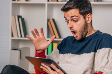 young man at home with tablet or laptop with surprised expression