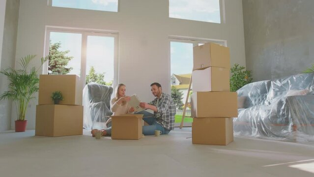 A young couple bought new house. The family unpacking cardboard boxes and easy and fast service delivery into big modern home
