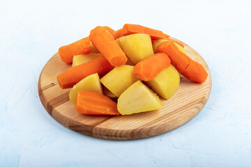 Boiled potatoes and carrots on a wooden cutting board.