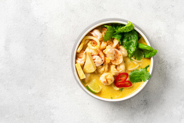 Asian laksa soup with shrimp in a ceramic bowl on a light culinary background. Spicy broth soup with coconut milk, rice noodles and seafood in a plate on the closeup kitchen table. Top view