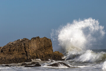 Large wave breaks on offshore rock near Malibu, California, sending ball of spray into the air,...