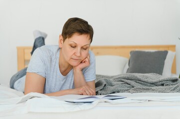 leasure and home concept - smiling middle-aged woman reading book and lying on couch at home.