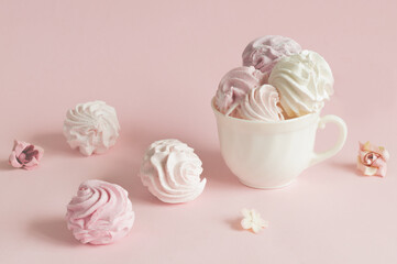 Sweet twisted marshmallow in pink tones, in a mug and scattered in a chaotic manner on a pink pastel. selective focus