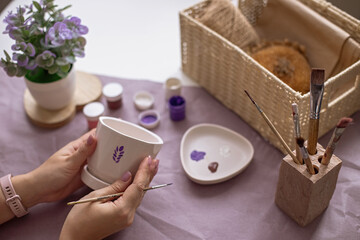 Womens hands hold a white flower ceramic pot on the table