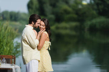 happy man touching cheek of smiling woman near lake.