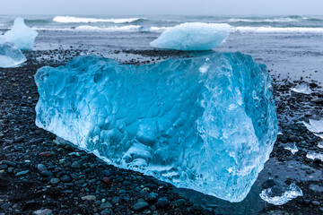 Ocean waves breaking over icebergs and large chunks of blue ice on a volcanic black sand beach (Diamond Beach, Iceland)