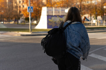 Fototapeta premium Rear view of unrecognizable teenage girl with backpack walking on street. A Young woman walks down city street, black backpack on his back.