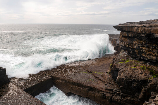 Dún Aonghasa and cliffs of Inishmore, Aran islands, county Galway, Ireland. Popular tourist landmark with stunning Irish nature scenery. Blue ocean and sky. Panorama image. Powerful ocean wave.