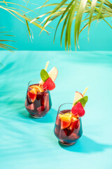 Glasses with traditional Sangria cocktail decorated with pieces of fresh strawberry, pinch of mint and eco-paper straw.