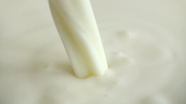 A pouring stream of milk into the milky surface. Slow motion.