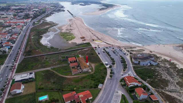 Esposende, Portugal, April 10, 2022: DRONE AERIAL FOOTAGE - The two sides of Restinga de Ofir. Esposende fishing harbor maintenance dredging. Dumper vehicles and rotating excavator parked on the sand.