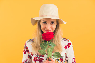 elegant blonde European girl holding a red rose and smiling medium closeup yellow background studio shot beauty concept. High quality photo