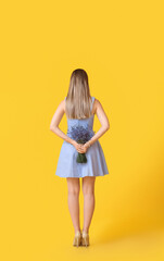 Beautiful young woman with bouquet of lavender on color background, back view