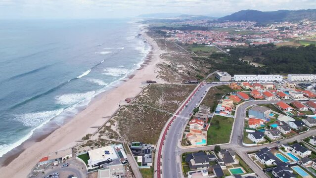 DRONE AERIAL FOOTAGE: Northern Littoral Natural Park in Esposende, Portugal. Sea, beach boulders, pebble shore, and waves. Sea waves breaking on rocks. Sunny beach with sand dunes and a cloudy sky.