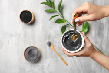 Woman preparing activated carbon facial mask on light background, closeup