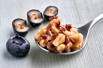 Spoon with cereal oatmeal and flax seeds surrounded by blueberries