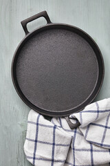 Empty round cast iron pan, tea towel on a light blue wooden table