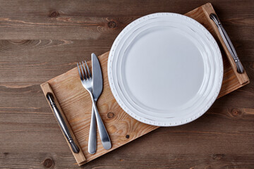 White ceramic plate and a wooden tray with cutlery on a brown wooden table