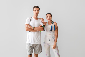 Sporty young couple with skipping ropes on grey background